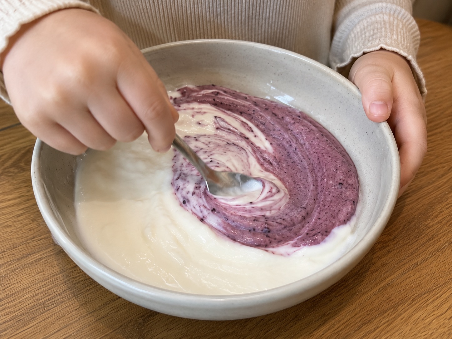 Kind roert wilde blauwe bes poeder door yoghurt tot een paarse swirl